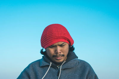 Portrait of young man wearing hat against clear blue sky