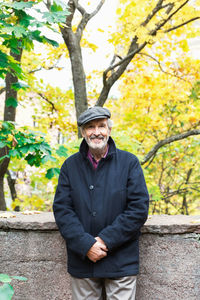 Portrait of happy senior man standing in park during autumn