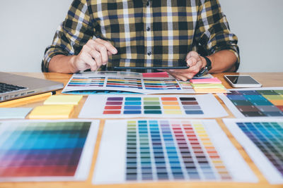 Midsection of creative occupation person using digital tablet with color swatches on table