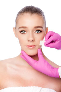 Cropped hands of doctor giving beauty treatment to young woman against white background