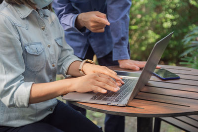 Midsection of businesswoman using laptop with colleague outdoors