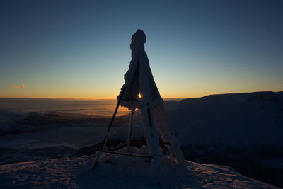 Silhouette people on snow covered land against sky during sunset