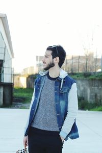 Young man looking away while standing against built structure