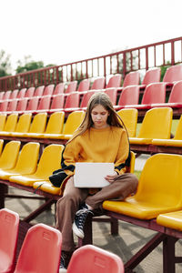 A young girl is doing her homework using a laptop in the stands of the stadium.