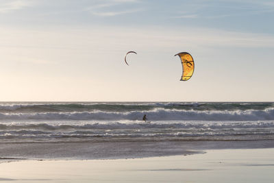 Distant view of person kiteboarding on sea against sky