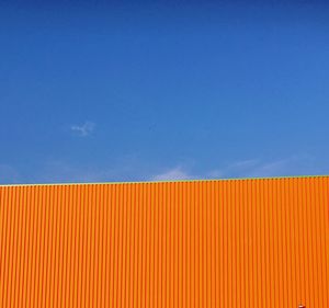 Low angle view of orange wall against blue sky