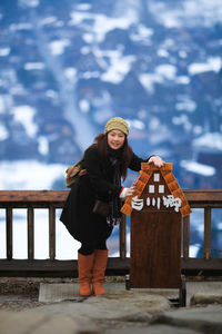 Full length portrait of woman standing by information sign during winter