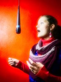 Young woman looking away while standing against red wall