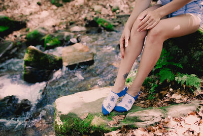 Young hipster girl sitting on a rock at river in forest in printed bright socks