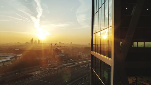 Reflection of sun on office building against sky during sunset