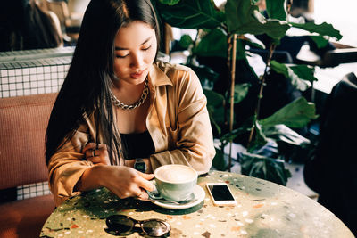 Young woman holding coffee while sitting on table at cafe