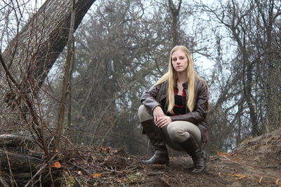 Portrait of woman crouching on land against trees