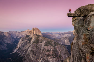 Scenic view of rocky mountains with man standing against sky during sunset