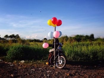 Man with motorcycle selling balloons on field against sky