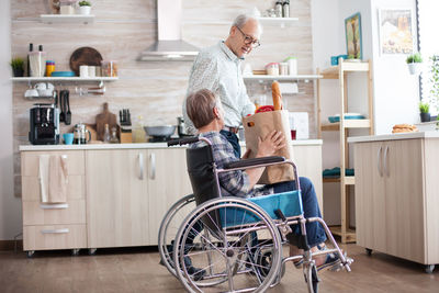 Woman sitting on wheelchair while standing at home