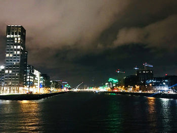 Illuminated buildings by sea against sky at night