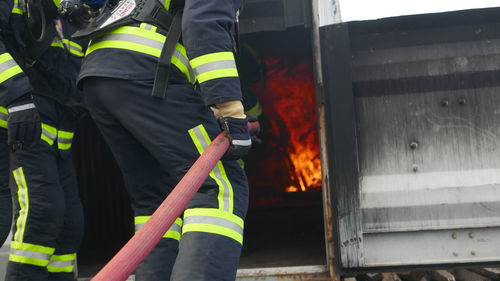 Rear view of firefighters in uniform spraying water against fire