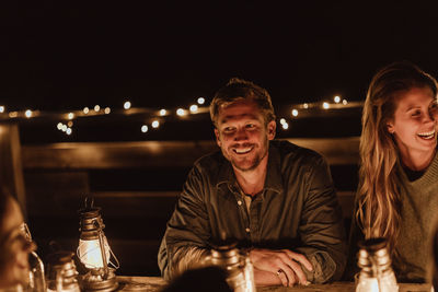 Smiling man sitting with female friend in restaurant at night