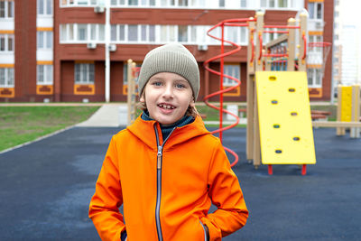 Funny caucasian blond boy in an orange jacket plays on the sports playground