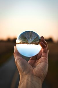 Close-up of hand holding crystal ball against sky