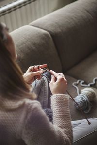 High angle view of woman knitting wool while sitting on sofa at home