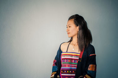 Young woman looking away while standing against wall