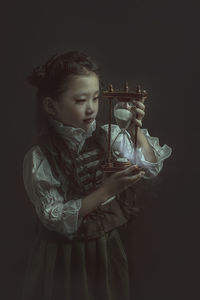 Girl wearing costume while holding hourglass against black background