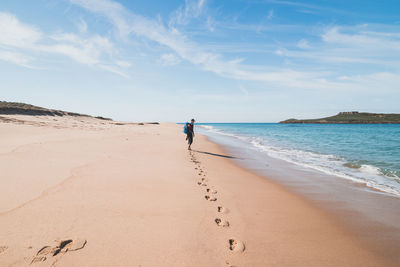 Rear view of woman walking at beach against sky