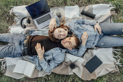 Pleased caucasian relaxed students lying near laptop,  break in park. work-life-balance concept