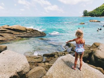 Rear view of boy standing on rock by sea against sky