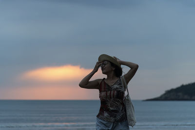 Woman standing at beach against sky during sunset