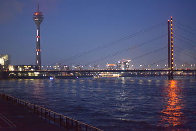 Illuminated bridge over river against sky in city