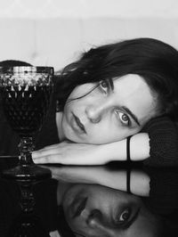 Portrait of young woman lying by drinking glass on table