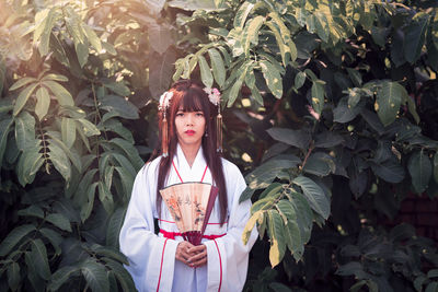 Portrait of young woman standing against plants