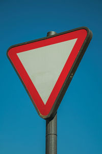 Low angle view of road sign against clear blue sky