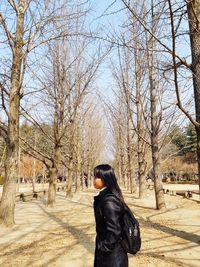 Side view of woman standing by bare trees on field 