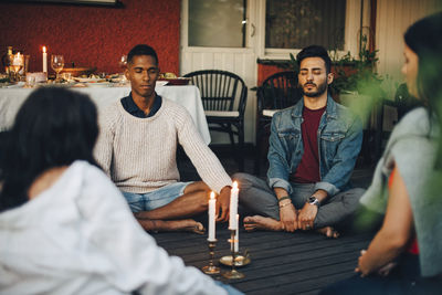 Multi-ethnic male and female friends sitting with eyes closed in balcony during group session