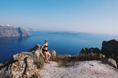 Woman leaning on rock at cliff against sea