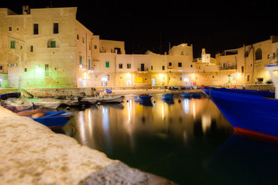 Boats moored in canal amidst buildings in city at night