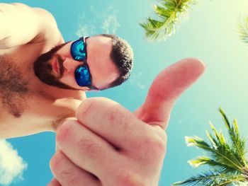 Directly below shot of shirtless man showing thumbs up sign against sky