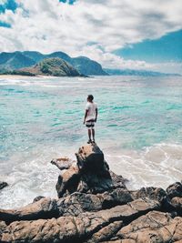 Woman standing on rock by sea against sky