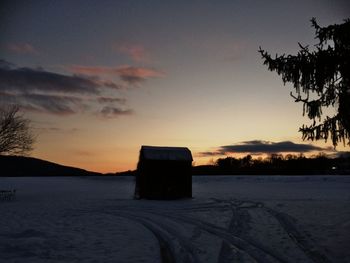 Silhouette built structure on snow covered landscape against sky at sunset