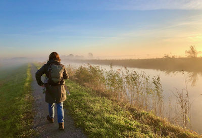 Rear view of a woman walking along a little river in a rural landscape at sunrise