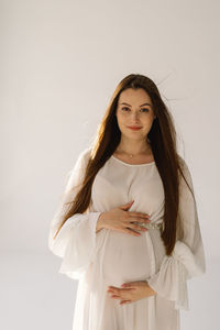 Cute young pregnant girl sitting on the white studio in warm light