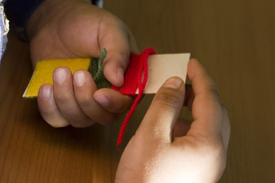 Cropped hands of boy holding strip with woolen strings on table