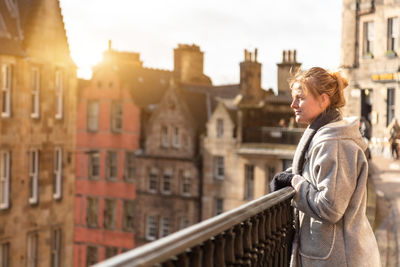 Side view of woman standing by railing against building