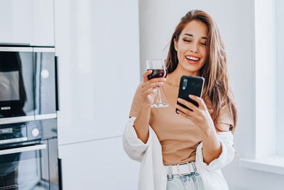 Young woman using phone while standing on laptop