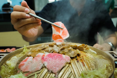 Midsection of man holding meat with chopsticks at restaurant