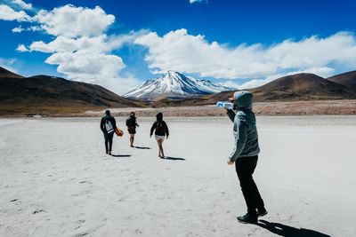 Rear view of people walking on snowcapped mountain against sky