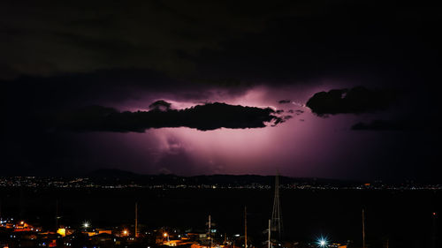 Scenic view of illuminated city against dramatic sky at night